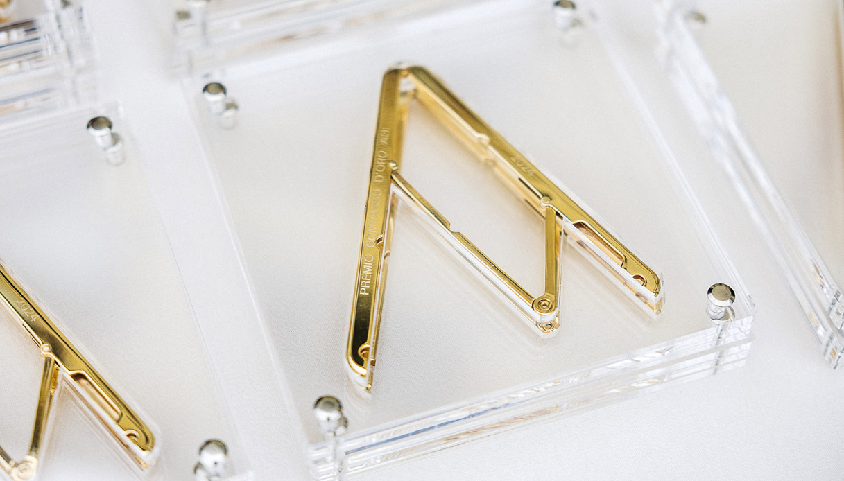 Trofeo del Premio Compasso d'Oro ADI con compasso in metallo dorato racchiuso in teca in plexiglass trasparente su fondo bianco