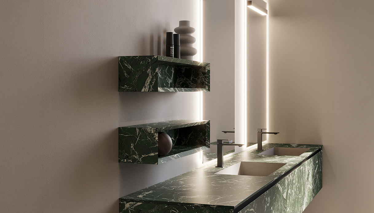 Bagno con piano lavabo e mensole a parete in gres Verde Dolomite con venature chiare, rubinetti bronzo scuro e specchio con retroilluminazione verticale su parete beige