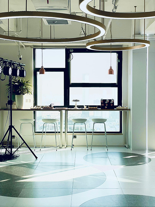 Spazio aperto con grandi finestre, anelli luminosi dorati sospesi al soffitto, lampade a sospensione in rame e pavimento con motivi geometrici