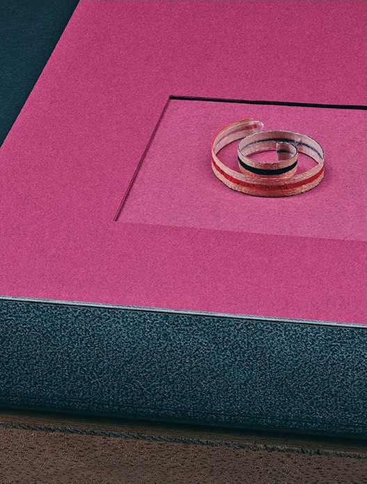 Opera di Haruka Misawa con spirale in materiale trasparente posata su superficie in carta magenta con riquadro incassato, su base grigio scuro