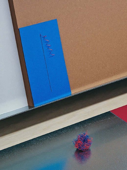 Opera di Haruka Misawa con carta blu cucita da filo zigzag rosso-blu appoggiata su cartone, e piccola sfera di filo colorato sul piano metallico