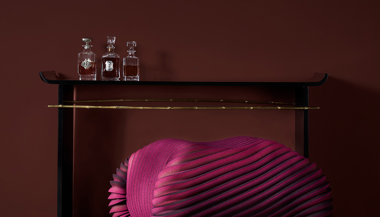 Consolle nera con mensola e barra in ottone effetto bamb&ugrave;, tre decanter in cristallo e plaid fucsia pieghettato appoggiato sotto, allestimento Nilufar Grand Hotel Depot Milano