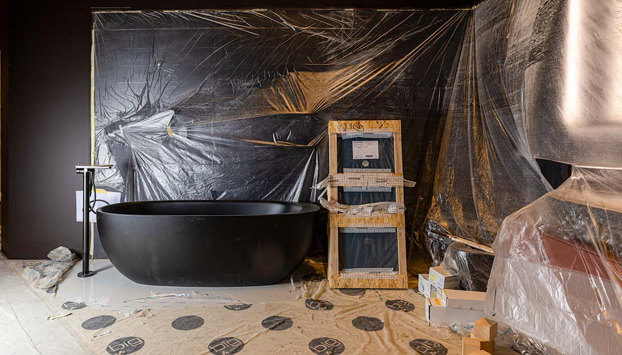 Vasca freestanding nera opaca gi&agrave; posizionata in uno stand del Salone Internazionale del Bagno ancora avvolto da teli di protezione durante il making of del Salone del Mobile 2026
