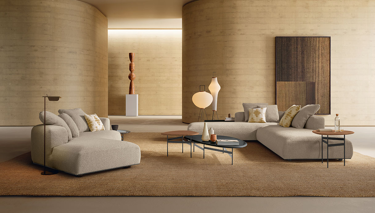 Salotto con due divani modulari Paco Talenti Home in boucl&eacute; beige chiaro, tavolini ovali in metallo nero con piano in legno e moquette in fibra naturale, pareti con colonne cilindriche in travertino