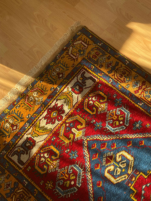 Angolo di tappeto kilim con motivi geometrici multicolori in rosso, blu, giallo e avorio posato su parquet in legno naturale caldo con luce solare radente