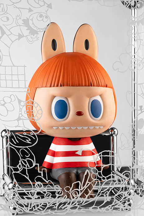 Primo piano della figura di Labubu Bob con capelli arancioni e maglia a righe rosse e bianche seduta su seduta in miniatura USM, con sfondo illustrato da Kasing Lung