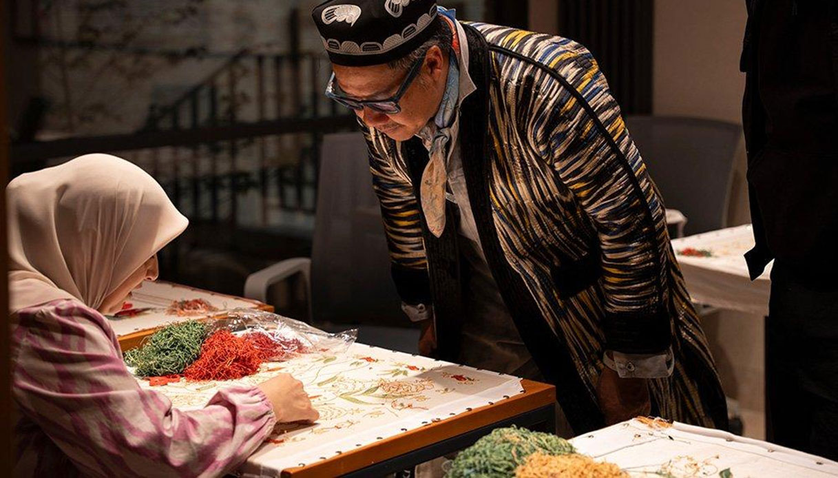 Kulapat Yantrasast osserva un'artigiana uzbeka con hijab che ricama a mano in un laboratorio di Tashkent, fili colorati sul telaio