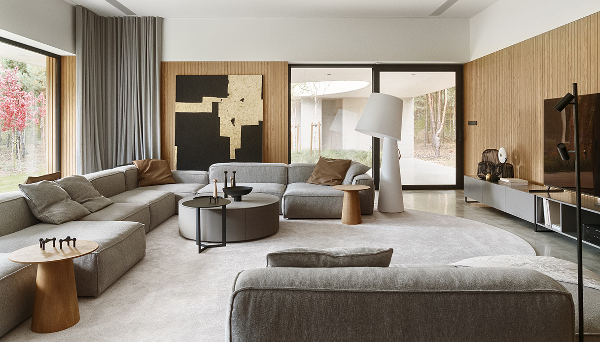 Living con divano modulare grigio, tela astratta in nero e oro e pareti in legno.