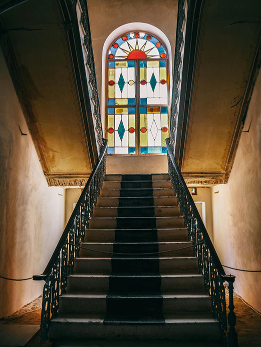 Scala storica con ringhiera in ferro e vetrata colorata ad arco a motivi geometrici