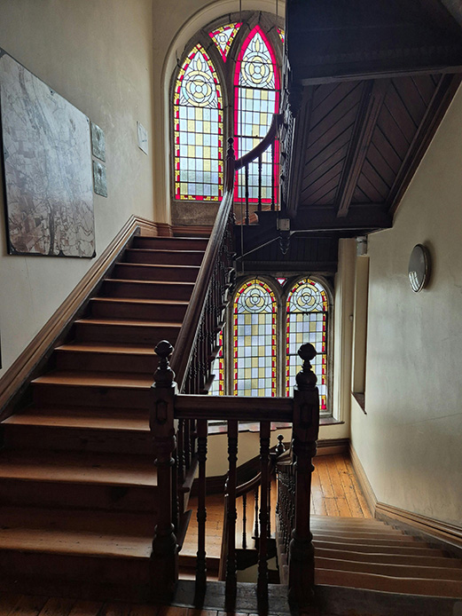 Scala a doppia rampa in legno con bifore gotiche e vetrate colorate a piombo