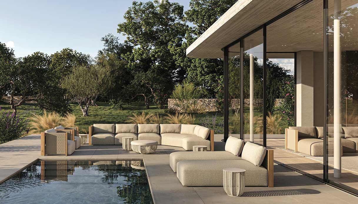 Sistema modulare di sedute outdoor in tessuto beige con struttura in legno chiaro attorno a piscina a sfioro, con grande vetrata che continua verso l'interno
