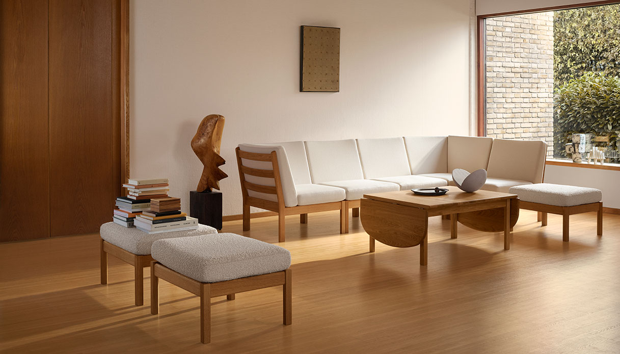 Living luminoso con divano modulare CH280 di Wegner in rovere oliato e tessuto bianco avorio, due pouf coordinati, tavolino CH086 in rovere con prolunghe a ribalta e scultura in legno grezzo su piedistallo scuro