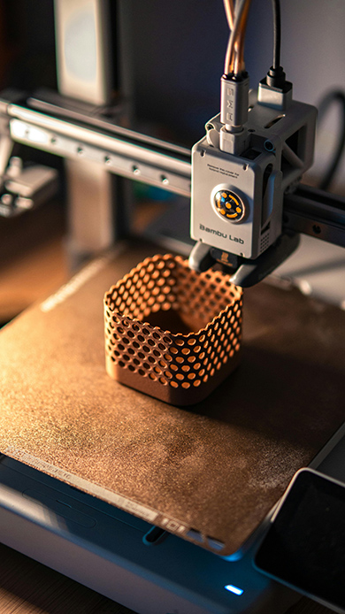 Stampante 3D Bambu Lab in fase di stampa di un oggetto reticolare esagonale color rame su piano di stampa illuminato