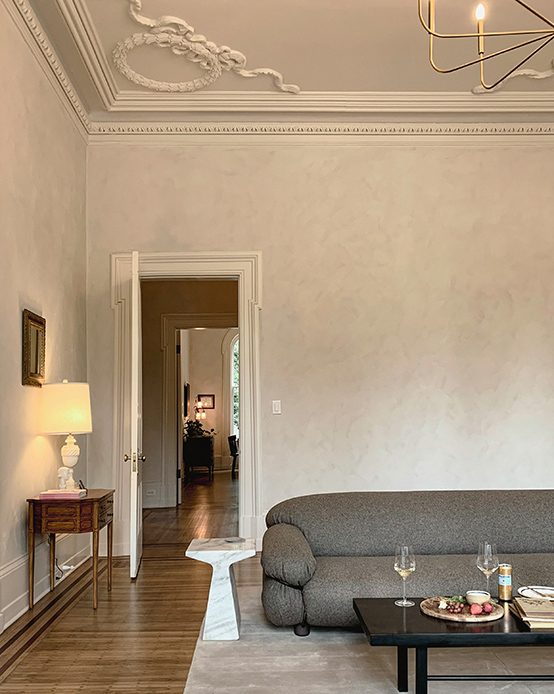 Soggiorno con pareti in stucco veneziano grigio, soffitto con decorazioni in gesso bianco, divano grigio antracite, tavolino in marmo e lampadario in ottone