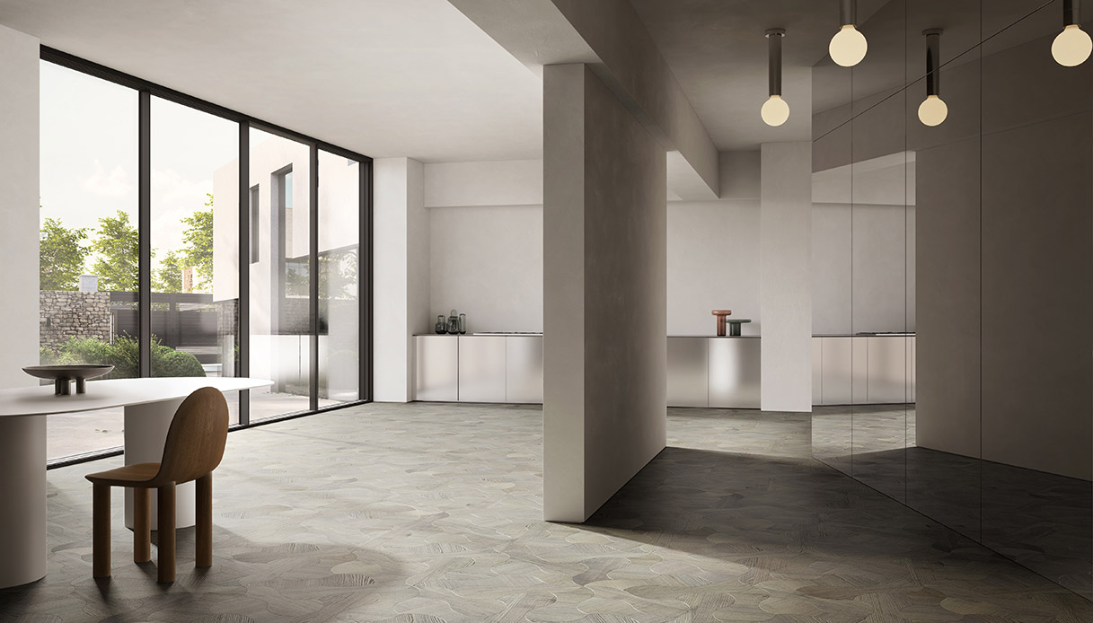 Ampio living con pavimento in parquet Supernova Listone Giordano in frassino grigio con pattern multidirezionale, sedia in legno chiaro, tavolo rotondo bianco e lampade a sospensione a sfera su sfondo con vetrate e cucina a specchio
