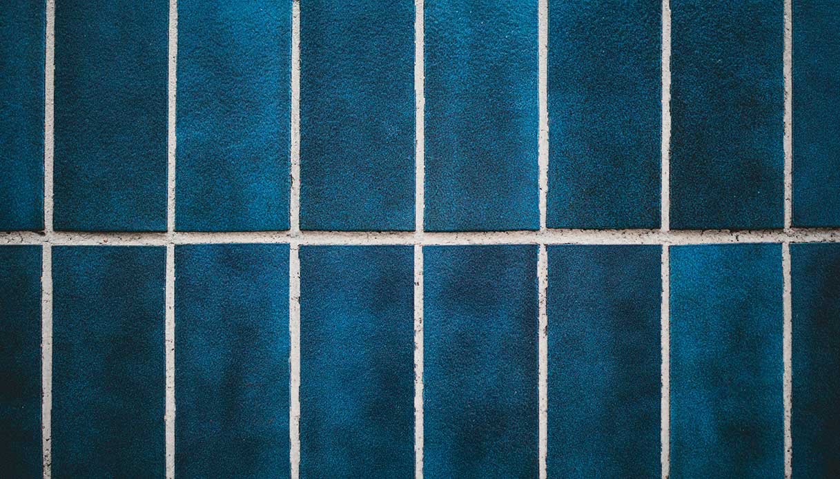 Dettaglio di parete con piastrelle rettangolari in ceramica blu scuro opaco con fughe bianche a contrasto in posa orizzontale sfalsata, texture granulosa della superficie in evidenza