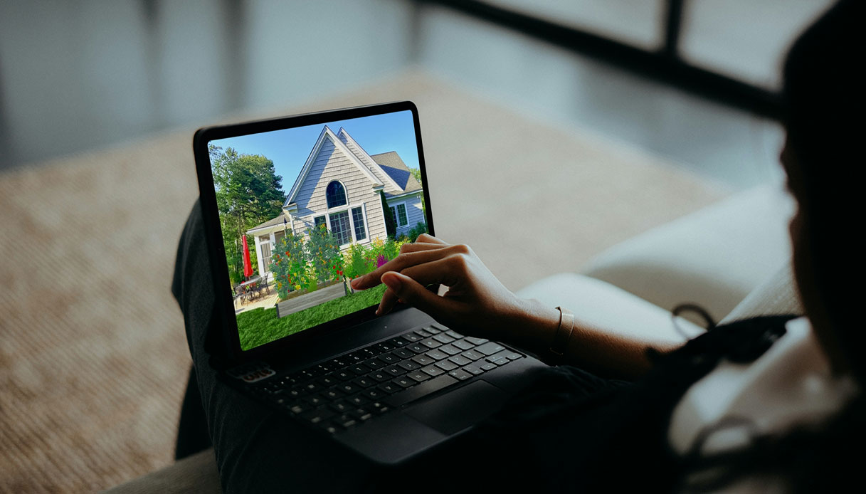 Persona che interagisce con un tablet mostrando il rendering 3D di un giardino residenziale con aiuole fiorite e patio