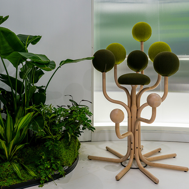 Appendiabiti dal design organico con struttura in legno curvato a forma di albero e sfere imbottite in verde muschio, accanto a piante tropicali