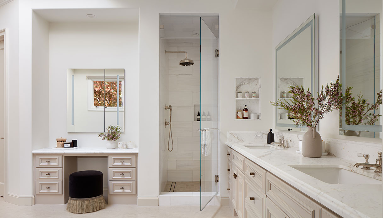 Bagno padronale con toeletta integrata a sette cassetti, doccia a pioggia con porta in vetro e doppio lavabo in marmo Calacatta con rubinetteria in nichel lucido