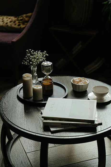 Coffee table rotondo scuro con vassoio, candele, libri impilati e piccoli oggetti decorativi