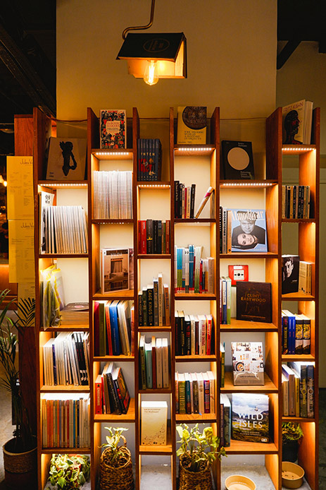 Libreria modulare in legno scuro con vani a giorno retroilluminati a LED, libri disposti in verticale e orizzontale, lampadina a filamento a sospensione