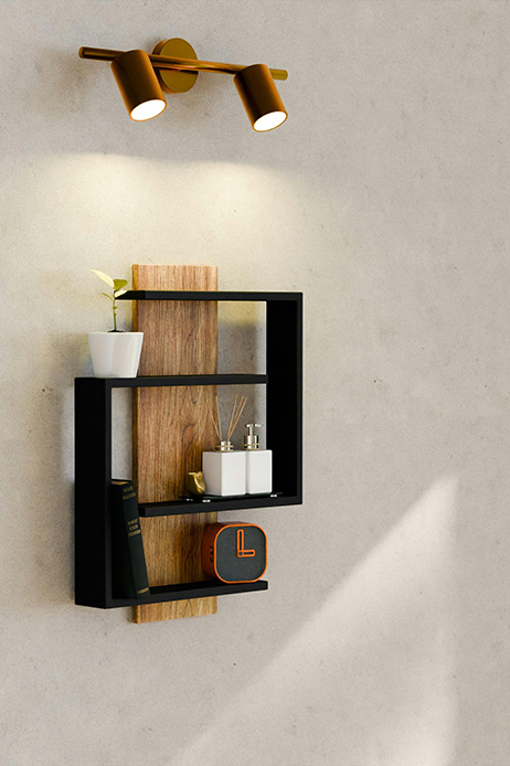 Mensola geometrica con struttura in metallo nero e ripiani in legno naturale su parete in stucco beige, con applique a due faretti in ottone sopra