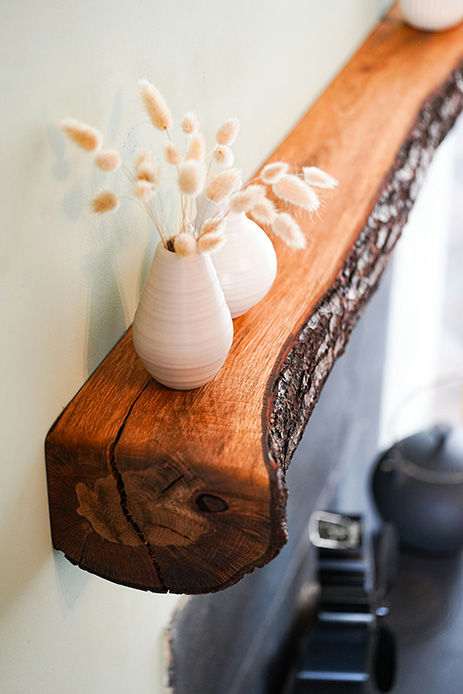 Mensola in legno live edge con corteccia naturale a vista, due vasi in ceramica bianca con erbe di pampa essiccate