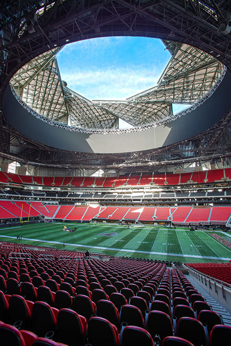 Vista interna del Mercedes-Benz Stadium di Atlanta con l'apertura circolare del tetto che lascia entrare la luce naturale, tribune rosse e campo verde