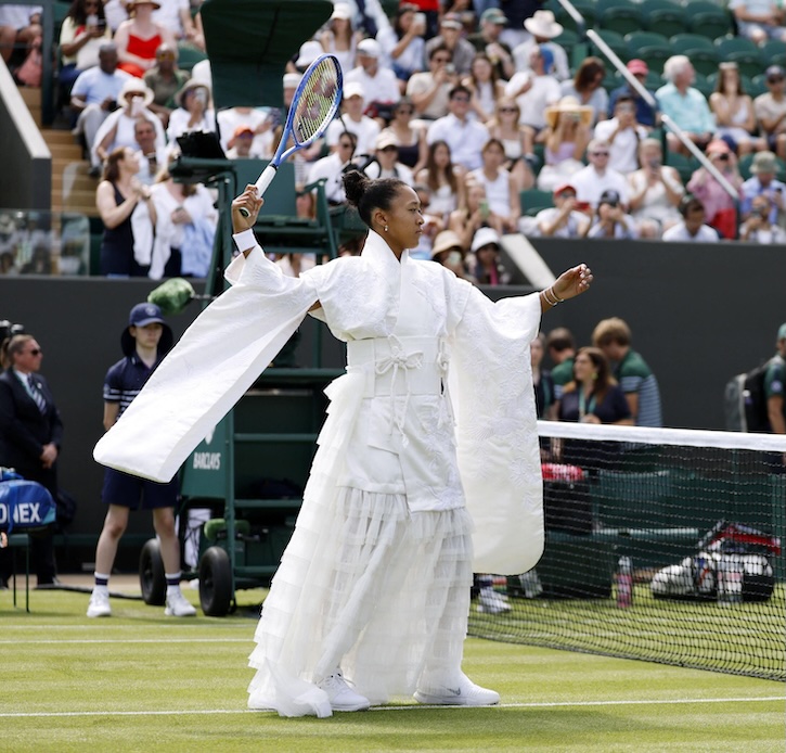 Naomi Osaka a Wimbledon con kimono bianco ricamato, maniche ampie e racchetta da tennis in mano