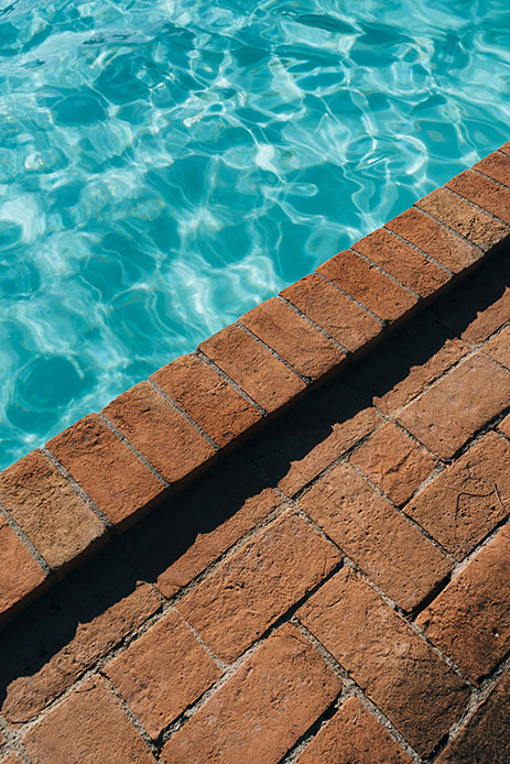 Dettaglio bordo piscina con mattoni in terracotta rossa e acqua turchese con riflessi luminosi
