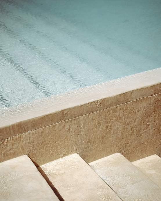 Dettaglio bordo piscina con gradini in pietra calcarea chiara color sabbia e acqua azzurra con riflessi luminosi