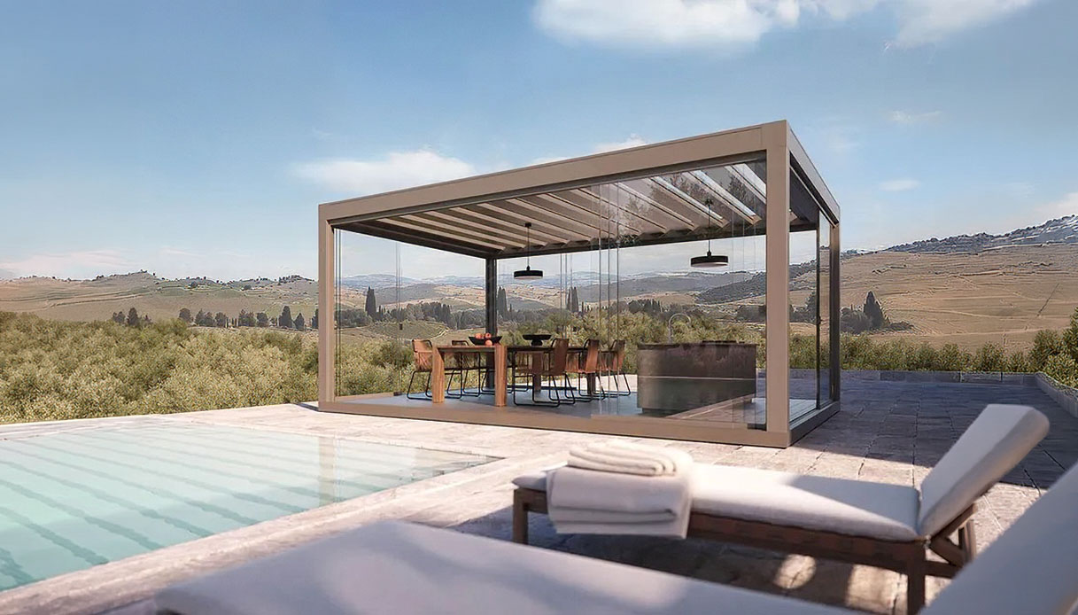 Pergola bioclimatica Pratic Carrera con lame orientabili in alluminio e vetrate perimetrali a scorrimento, su terrazza con piscina e panorama collinare
