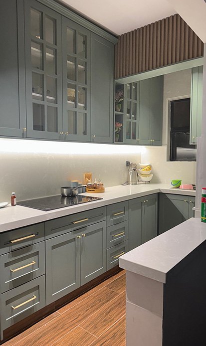 Cucina con ante in stile shaker verniciate verde salvia, maniglie in ottone lucido, piano in pietra bianca e striscia LED sottopensile