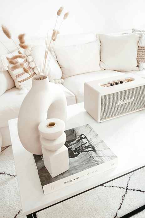 Tavolino bianco con vaso in ceramica, steli secchi, coffee table book e candela in stile monocromatico