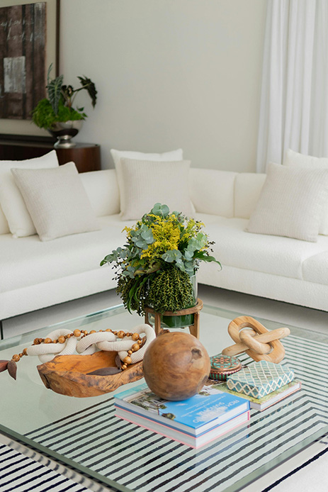 Tavolino in vetro con composizione di fiori freschi, oggetti in legno e coffee table book colorati