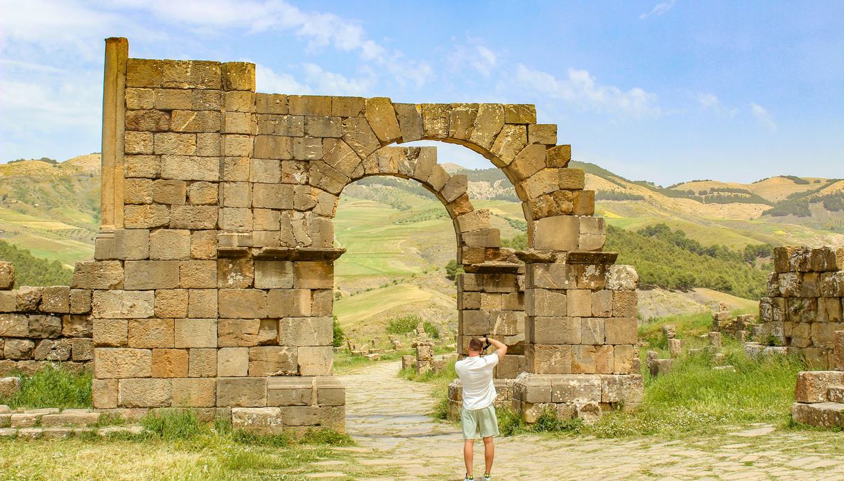 Arco romano in pietra tra le rovine di un sito antico, con colline verdi sullo sfondo