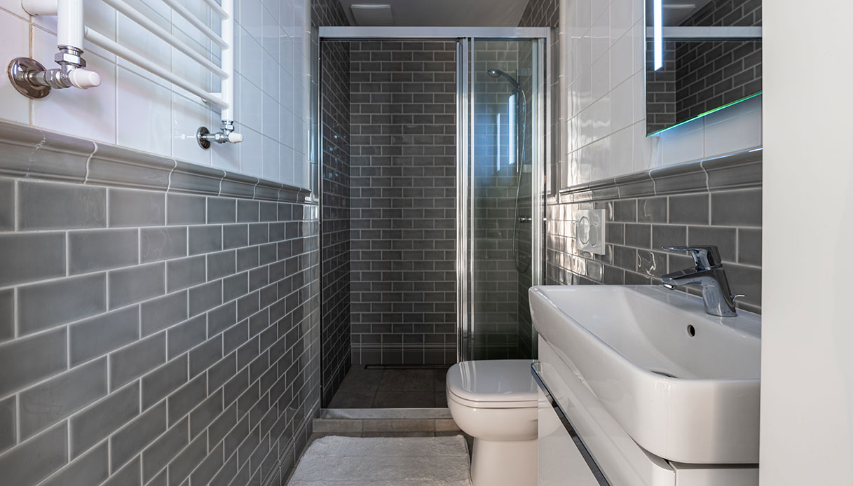 Bagno moderno con piastrelle grigie a effetto mattonella, box doccia in vetro, sanitari e lavabo bianchi