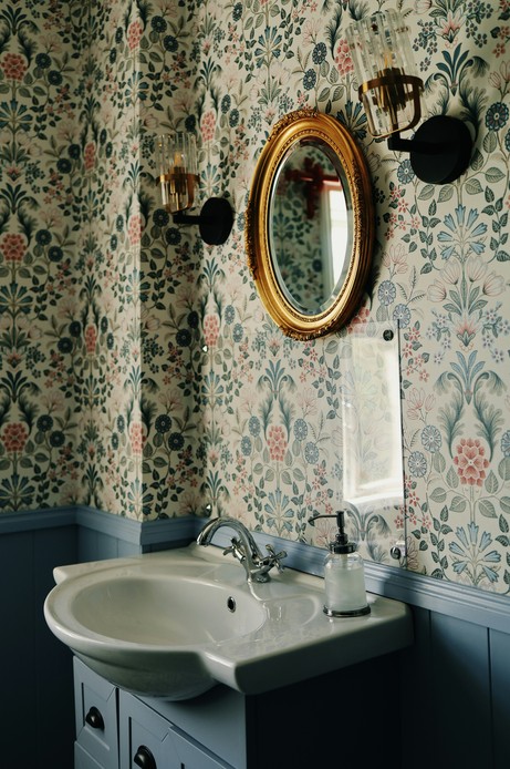 Bagno in stile vintage con carta da parati floreale multicolore, boiserie blu, specchio ovale dorato e rubinetteria cromata