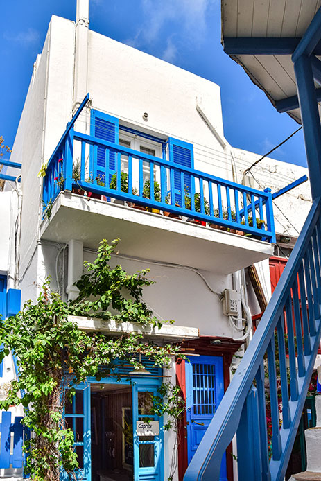 Balcone con ringhiera blu cobalto e persiane coordinate su facciata bianca, con rampicante verde e porta rossa