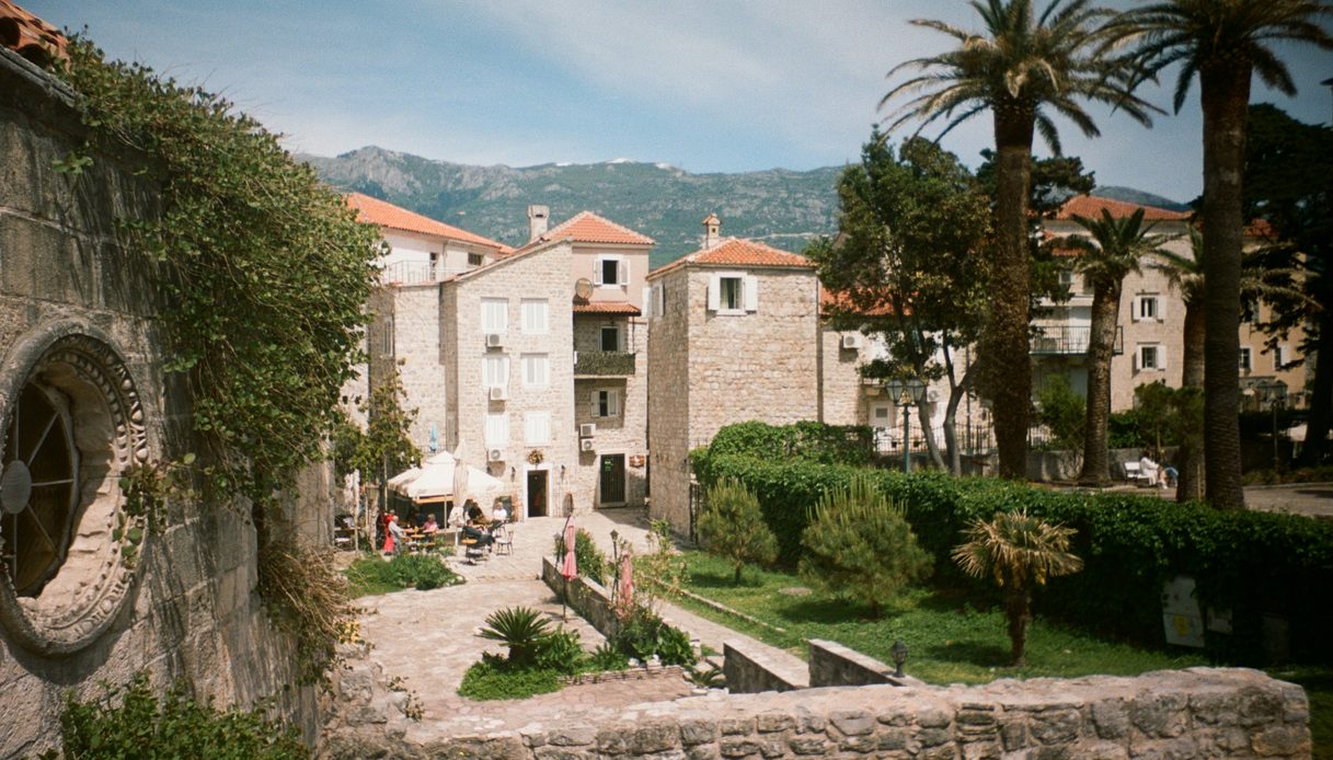 Borgo mediterraneo con case in pietra dai tetti in coppi, palme e montagne sullo sfondo