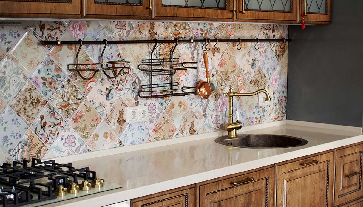 Cucina con rivestimento a piastrelle floreali patchwork, rubinetto e accessori in ottone, piano cottura a gas