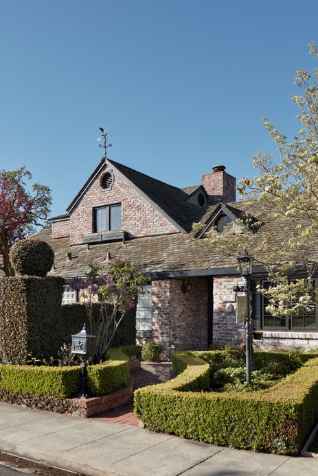 Facciata in mattoni di villa in stile Tudor con tetto in ardesia, siepi di bosso squadrate e glicine in fiore