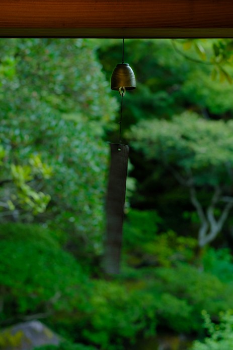 Campanella fūrin appesa a un filo sotto la grondaia, con un giardino verde e sfocato sullo sfondo