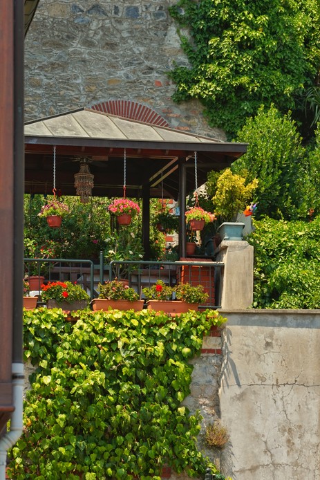 Gazebo con tetto a spiovente e cesti fioriti appesi, addossato a un muro in pietra ricoperto d'edera