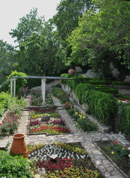 Giardino terrazzato con vialetti in pietra, aiuole geometriche, colonne di una pergola e giare in terracotta