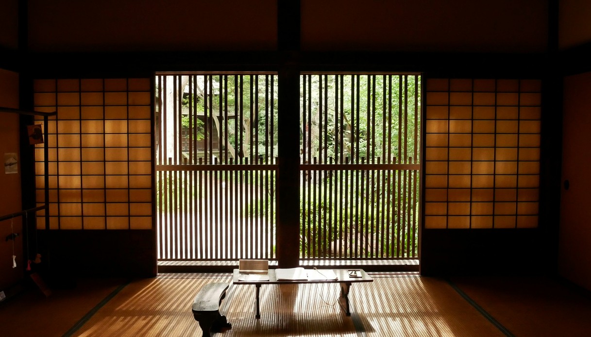 Interno tradizionale giapponese con pavimento in tatami, pannelli shoji e schermature in legno che si aprono sul giardino