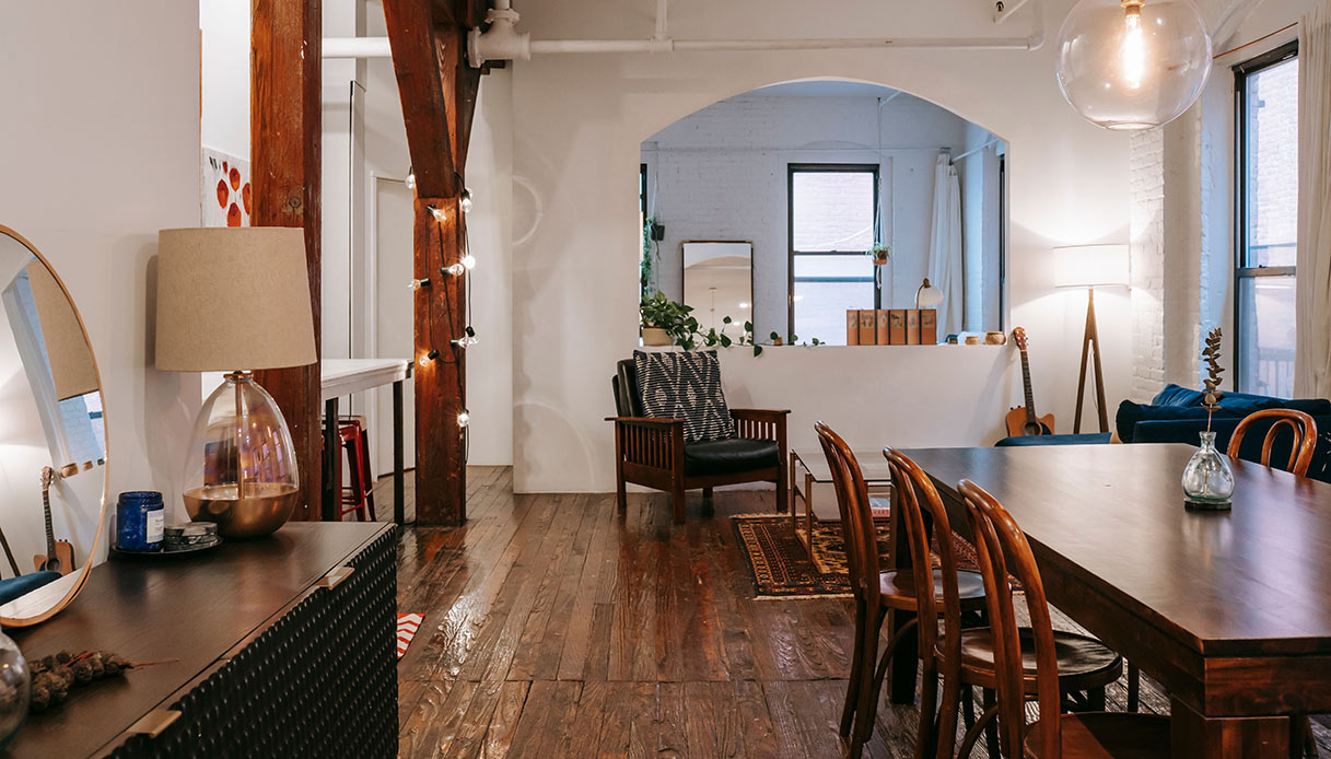 Soggiorno in stile loft con travi in legno a vista, lucine decorative, lampada da tavolo e lampadario a sospensione sferico