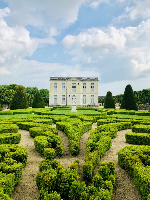 Palazzo francese con parterre in bosso disegnato a motivi geometrici, statua centrale e alberi a cono potati ai lati