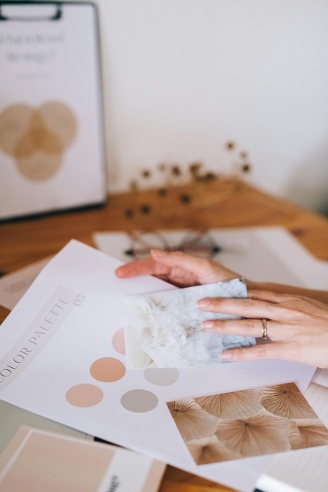 Mano che sfoglia una color palette con tonalit&agrave; terracotta e grigio, campioni di marmo e materiali naturali
