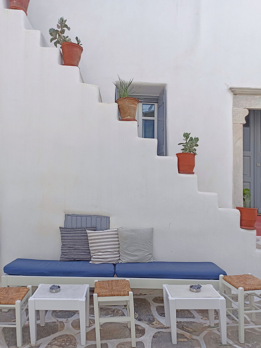 Panca blu con cuscini a righe addossata a una scalinata bianca decorata da vasi in terracotta con piante grasse